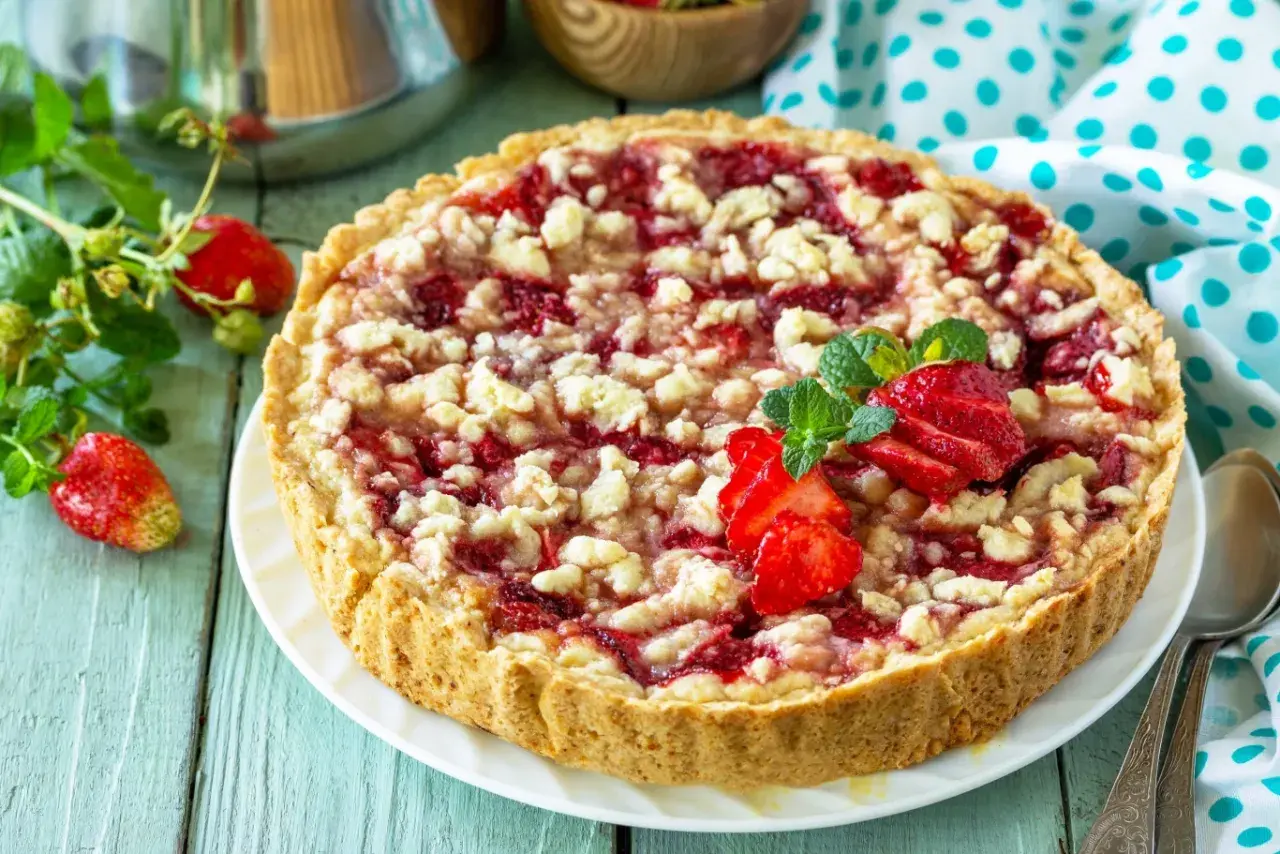 Pyszna tarta z truskawkami i kruszonką, ozdobiona świeżymi owocami i miętą, kusi apetycznym wyglądem.