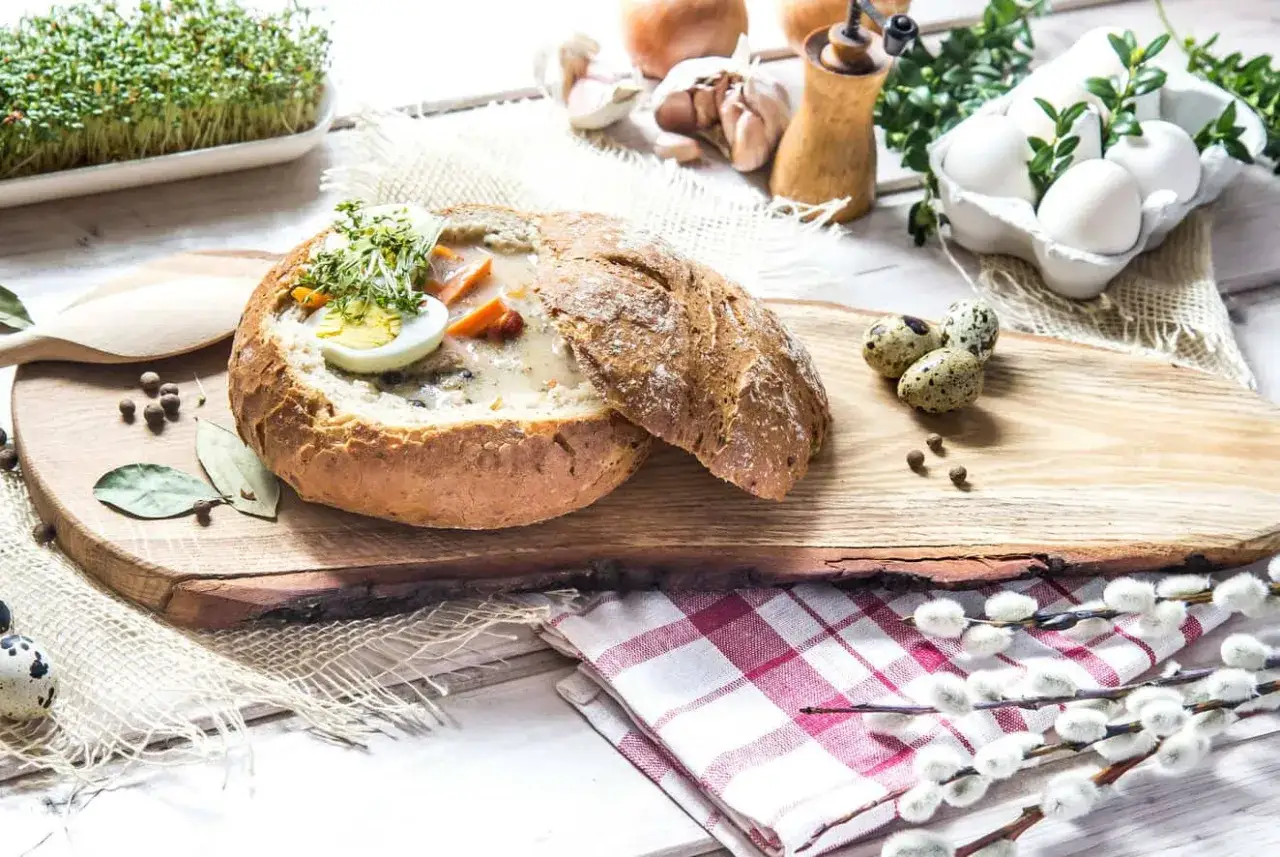 Tradycyjna zupa na wielkanoc w chlebie, ozdobiona jajkiem i kiełkami. Obok pisanki i bazie.