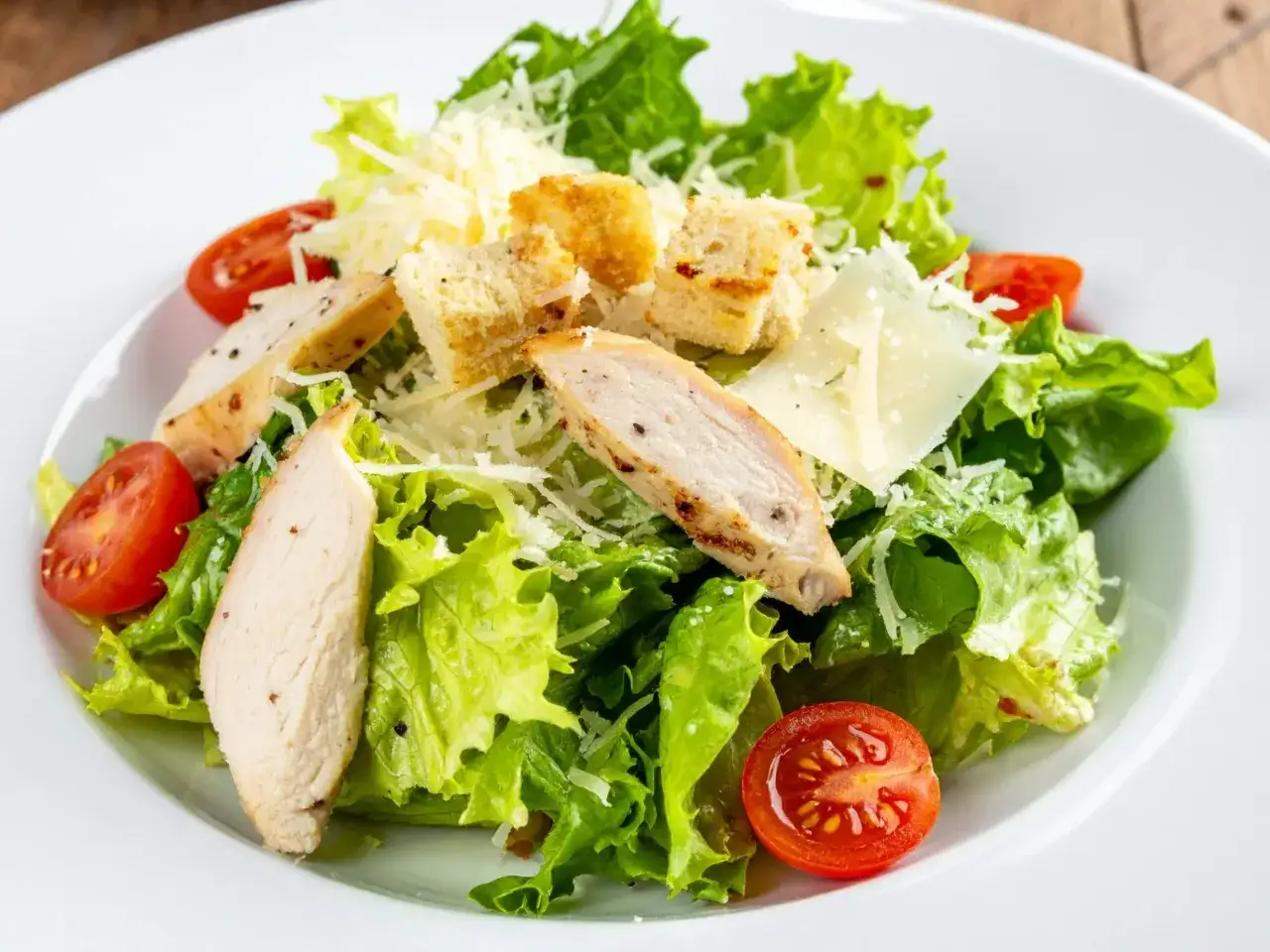 Pyszna surówka z sałaty rzymskiej z grillowanym kurczakiem, grzankami, pomidorkami i parmezanem.
