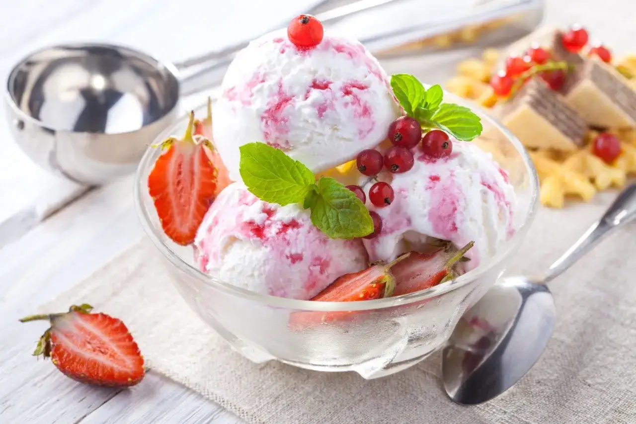 Pyszne lody z mascarpone, udekorowane truskawkami i porzeczkami, wyglądają jak letnie marzenie.