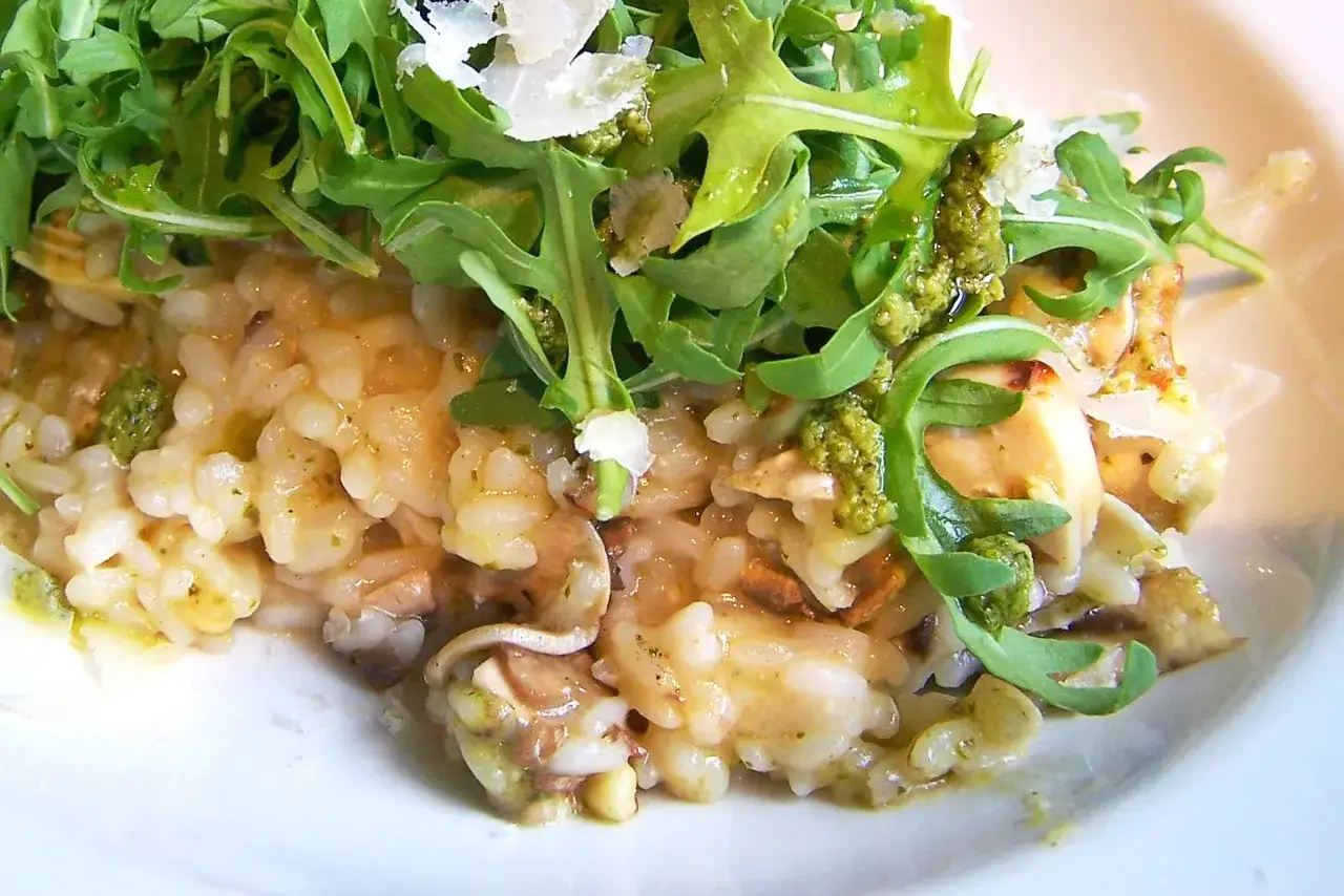 Kremowe risotto z pieczarkami, polane zielonym pesto i posypane parmezanem, ozdobione świeżą rukolą. Pyszne danie, które zachwyca smakiem.