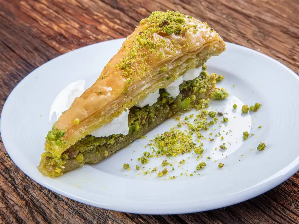 Pyszna baklava, co to? Warstwy ciasta filo, orzechów pistacjowych i słodkiego syropu na białym talerzu.