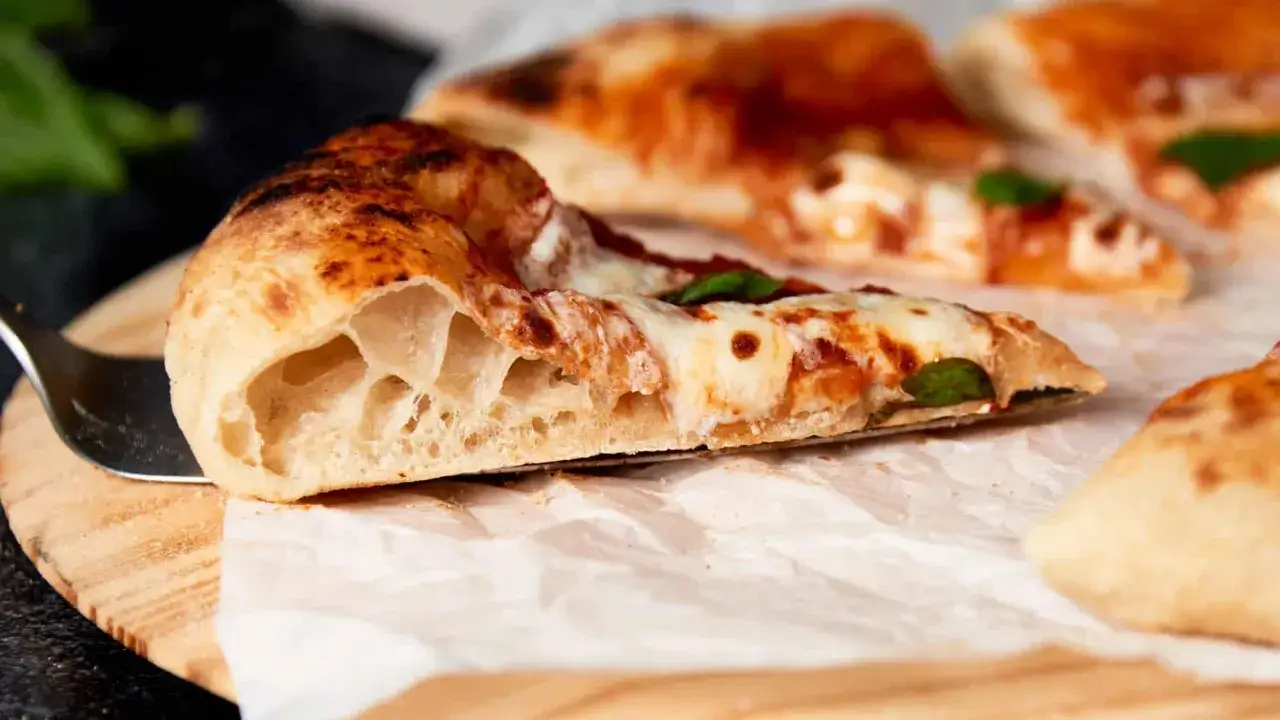 Kawałek puszystej margarita pizzy z rozpływającym się serem i aromatycznym sosem pomidorowym, gotowy do zjedzenia.