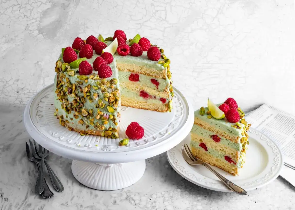 Pyszny tort z malinami i pistacjami. Kremowa masa pistacjowa otula biszkopt, a całość zdobią świeże maliny i limonka.