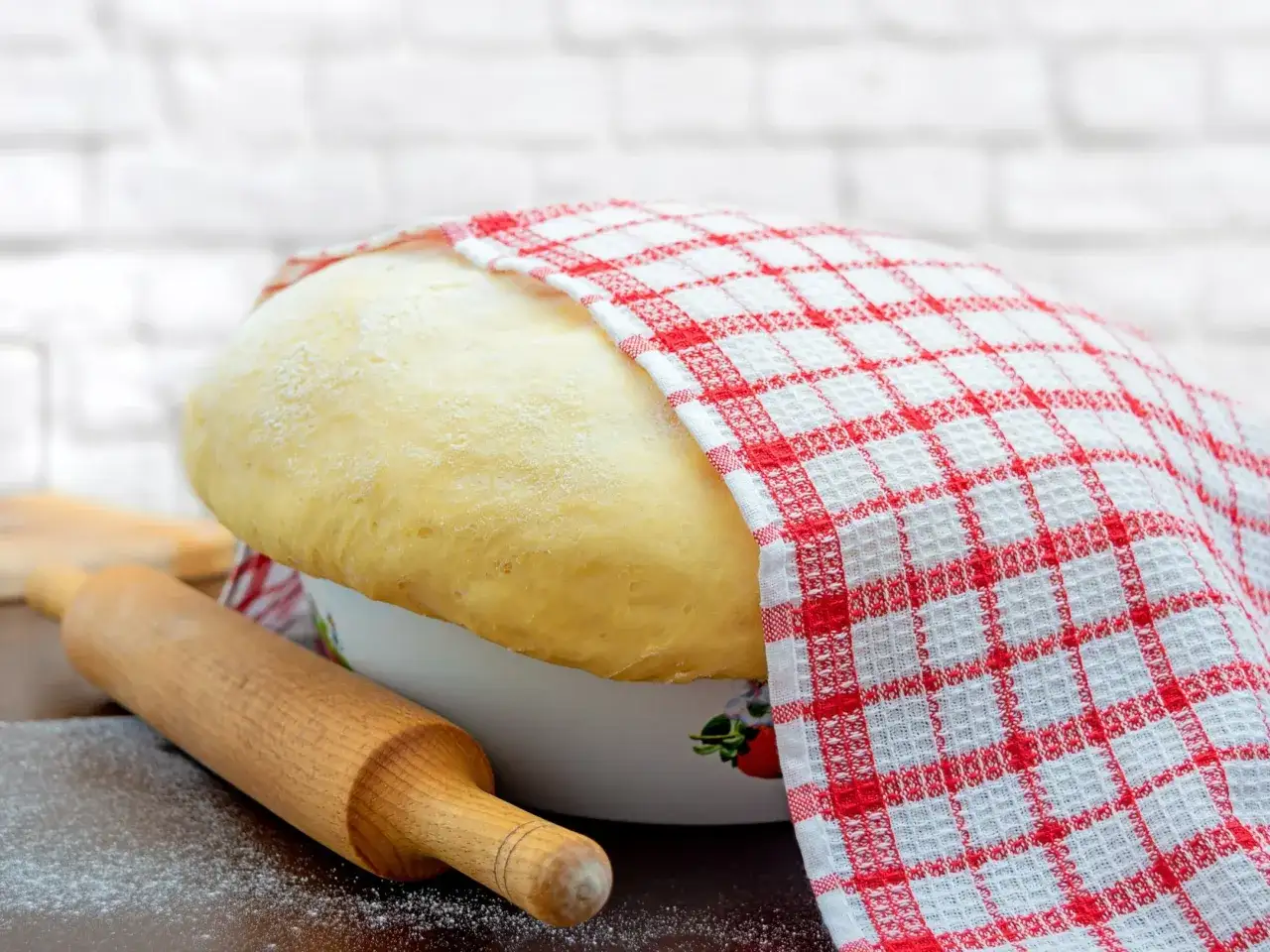 Wyrośnięte ciasto drożdżowe, przykryte ręcznikiem w kratkę, czeka na wałek. To sekretny przepis na ciasto drożdżowe babci.