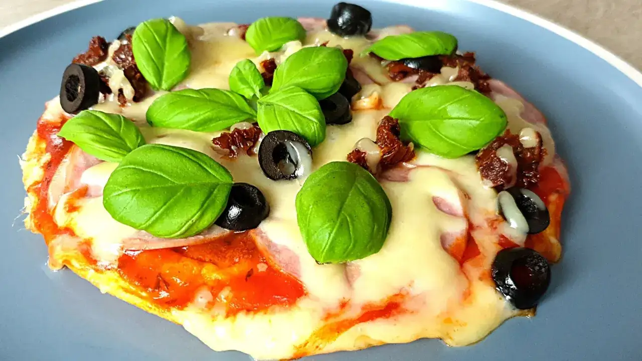 Szybki obiad keto: apetyczna mini pizza z mozzarellą, oliwkami, suszonymi pomidorami i bazylią.