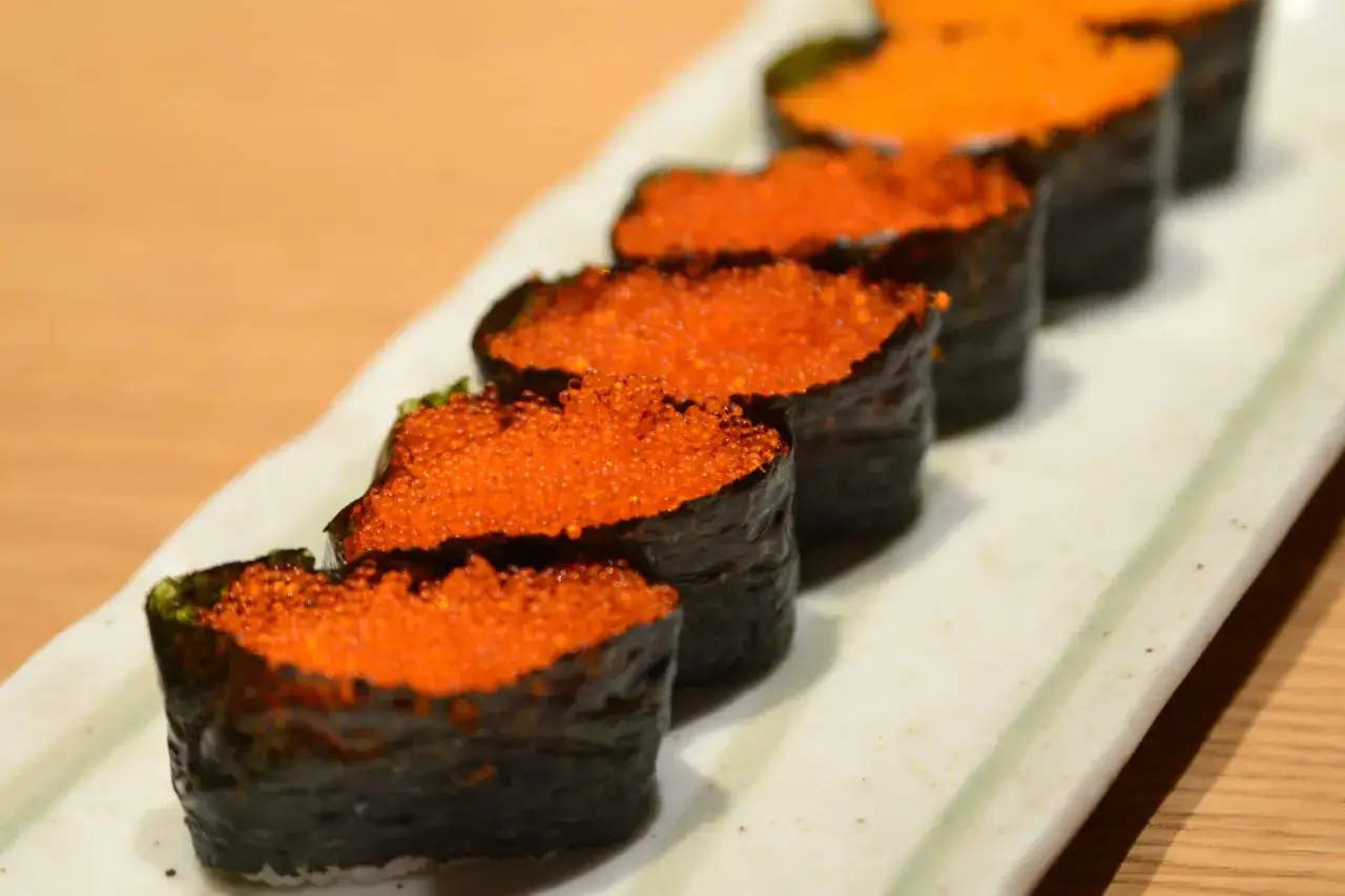 Rząd sushi gunkan maki z pomarańczowym tobiko, które błyszczy jak małe klejnoty na talerzu.