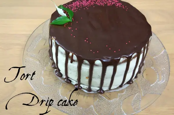 Pyszny tort drip cake z czekoladą spływającą po bokach, ozdobiony różową posypką i listkami.