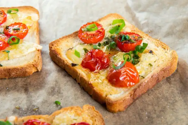 Pyszna, lekka kolacja: tosty z roztopionym serem, pieczonymi pomidorkami koktajlowymi i szczypiorkiem.