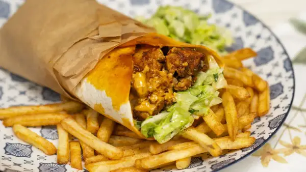 Pyszny kebab w tortilli z chrupiącymi frytkami i świeżą sałatką na talerzu.