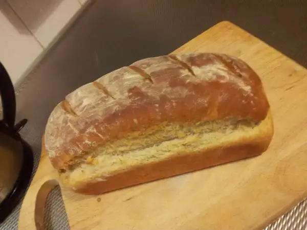 Pyszny, świeżo upieczony przaśny chleb z chrupiącą skórką, posypany mąką, leży na drewnianej desce.