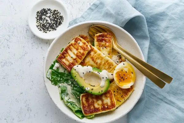 Szybki obiad keto: grillowany ser halloumi, awokado, jajko na miękko i zielone liście, posypane czarnym sezamem.