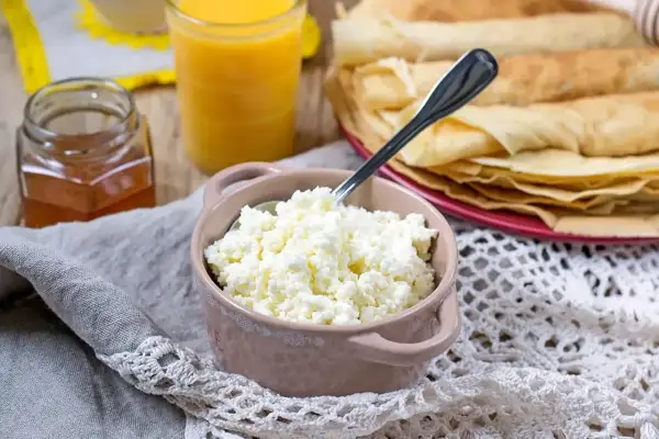Świeży twaróg, idealny do naleśników. Obok miód, sok i stos naleśników.
