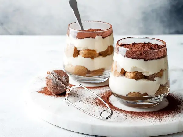 Dwa pucharki z kremowym tiramisu, posypane kakao. Idealna mizeria na słodko, która rozpływa się w ustach.