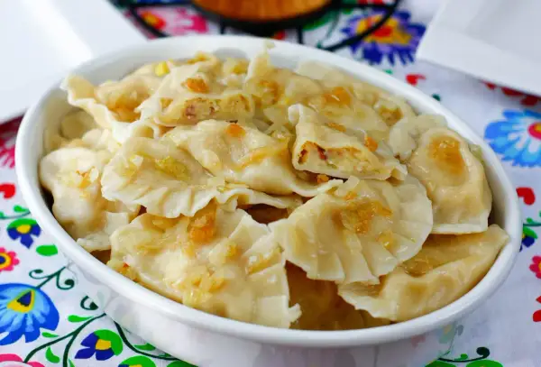 Pyszne pierogi ukraińskie z cebulką i skwarkami, podane w białej misce na kolorowym obrusie.