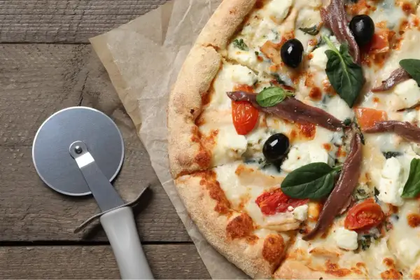 Pyszna pizza margarita z anchois, oliwkami i pomidorkami koktajlowymi, gotowa do pokrojenia.