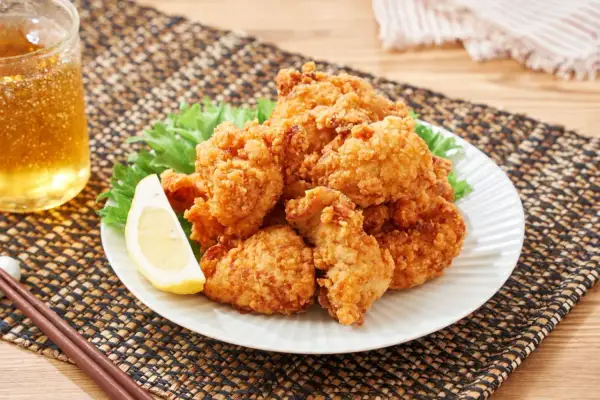 Chrupiące, złociste karaage na talerzu z sałatą i cytryną, obok szklanka piwa i pałeczki.