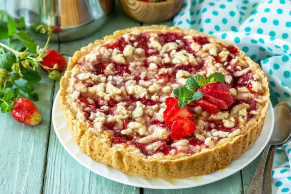 Pyszna tarta z truskawkami i kruszonką, ozdobiona świeżymi owocami i miętą, kusi apetycznym wyglądem.